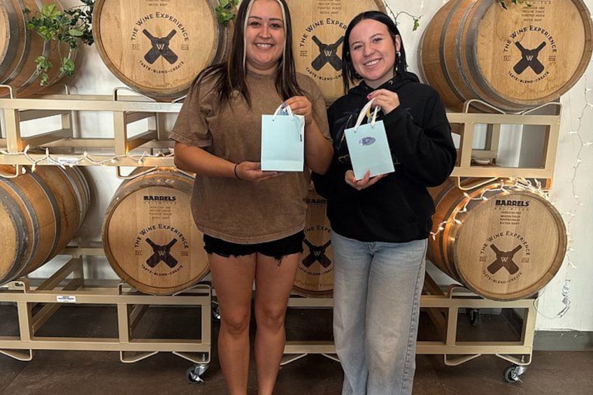 Two people holding light blue bags in front of wooden barrels with labels. 2