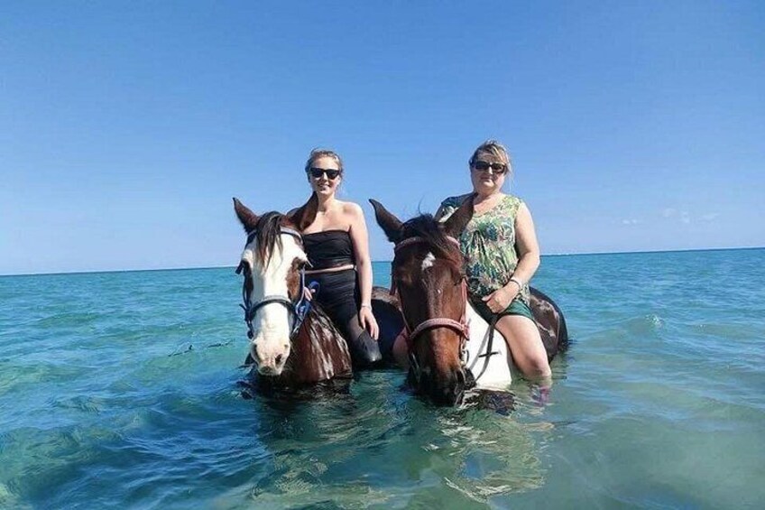 Two people riding horses in shallow water near the shore. 2