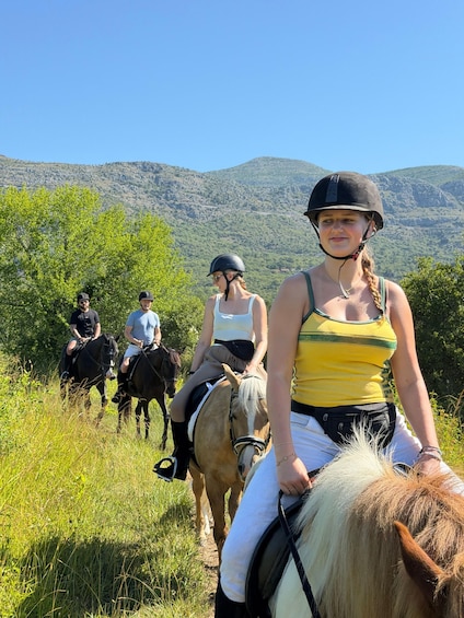 Three people riding horses on a trail with green trees and mountains in the background. 4