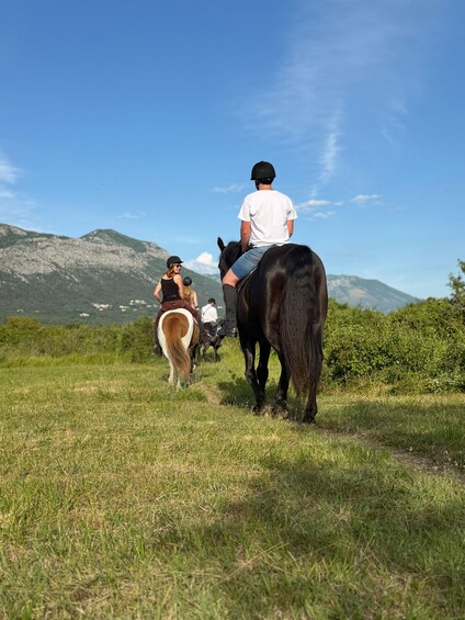 Three people riding horses on a grassy path with mountains in the background. 3