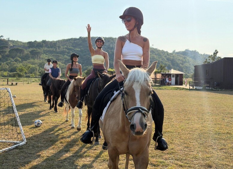 A group of people riding horses in an outdoor arena with a goal post and a barn in the background. 5
