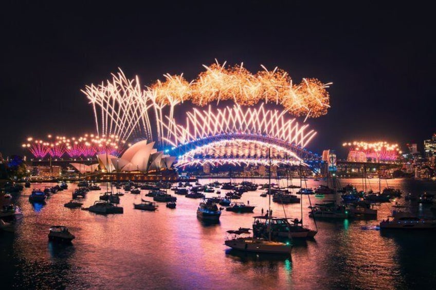 A nighttime view of the Sydney Opera House with fireworks above and boats on the water. 2