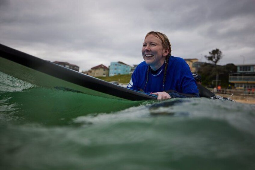 A person in a blue jacket leaning on a surfboard with a cloudy sky and buildings in the background. 4