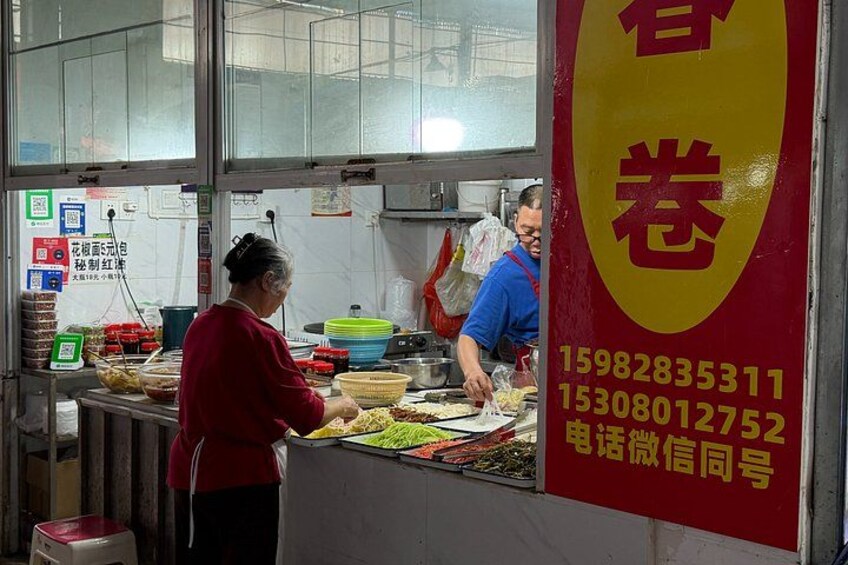 A food stall with a red and yellow sign, a person preparing food, and another person serving. 5