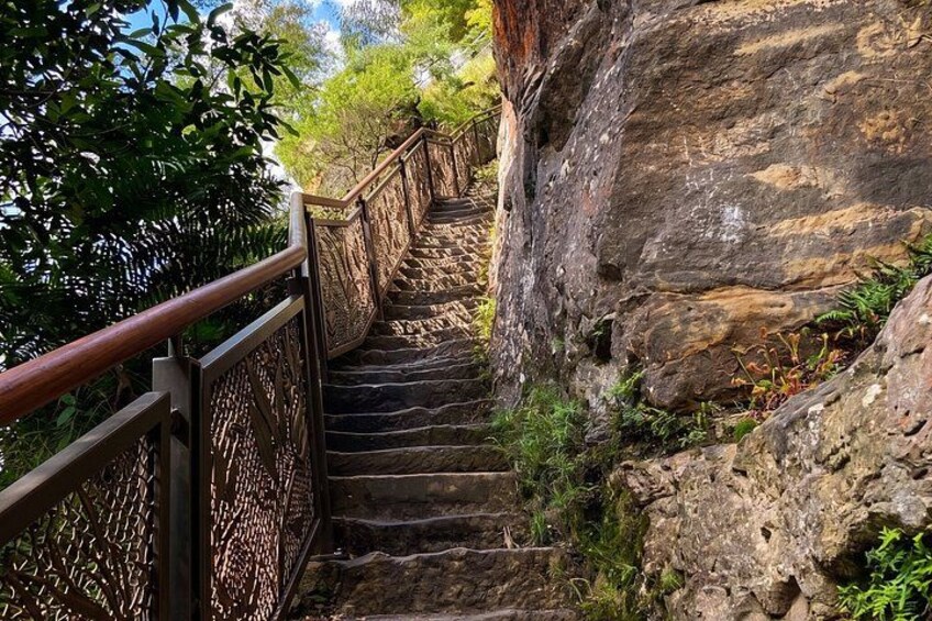 A stone staircase with metal railings descending a rocky slope, surrounded by greenery. 5