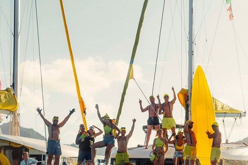 Un groupe de personnes se trouve sur un bateau à voile jaune, portant des chapeaux et des shorts, sous un ciel dégagé. 3