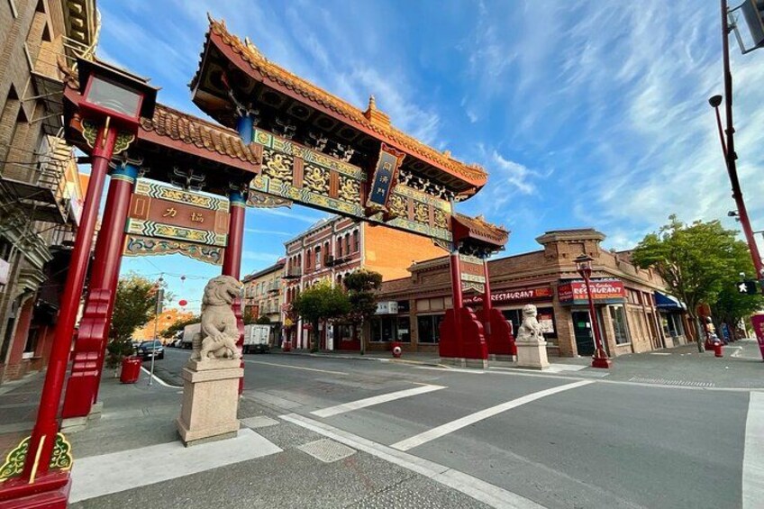 A street with a traditional Chinese gate, a lion statue, and a restaurant. 2