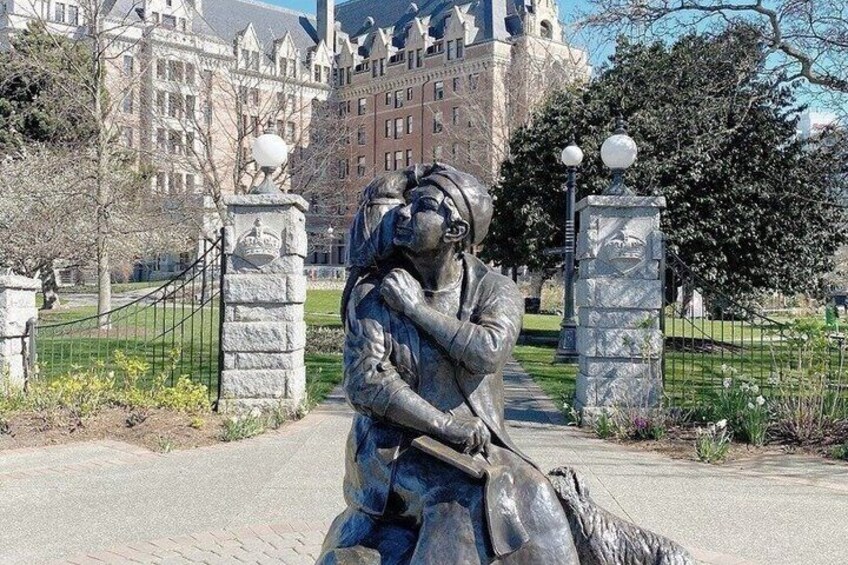 A statue of a man with a cane, a stone fence, and a large building in the background. 5