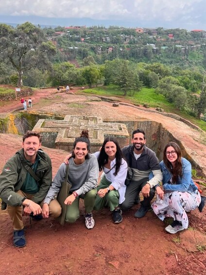 A group of people posing in front of a historical site with a stone structure and a view of a green landscape with scattered houses. 4