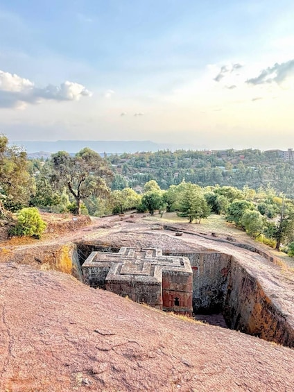 A large stone structure with a maze-like design, surrounded by a hilly landscape and trees. 1