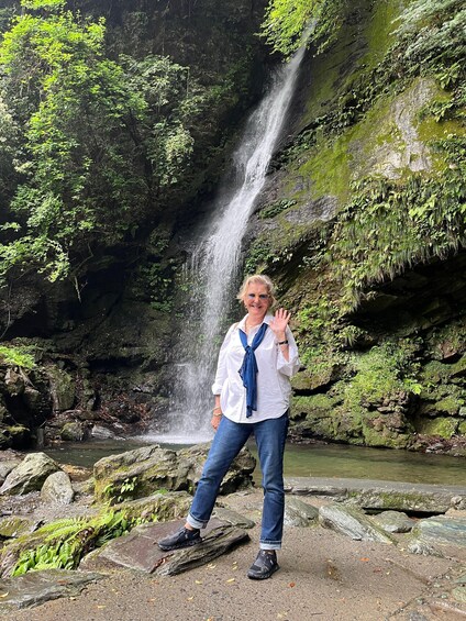 A person standing in front of a waterfall with lush greenery and a rocky terrain. 4