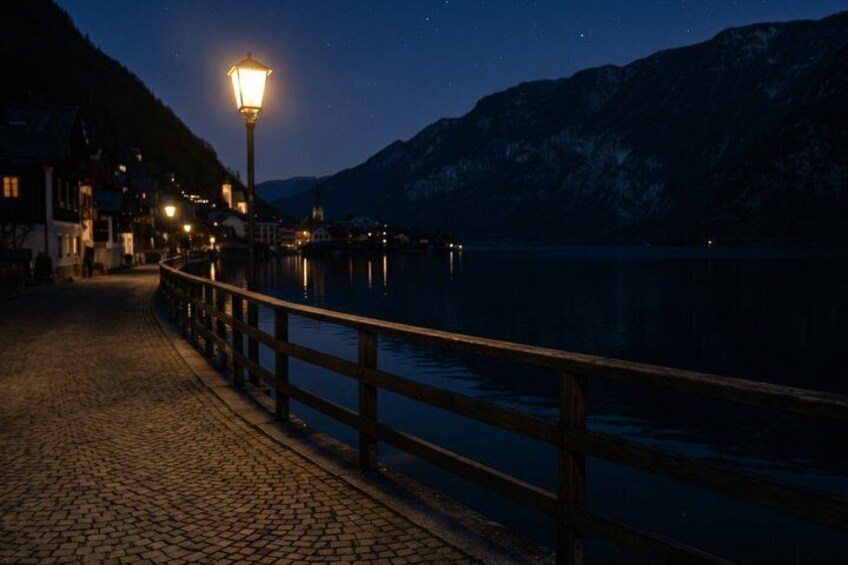 A nighttime lakeside walkway with a wooden railing, a street lamp, and buildings in the background. 5