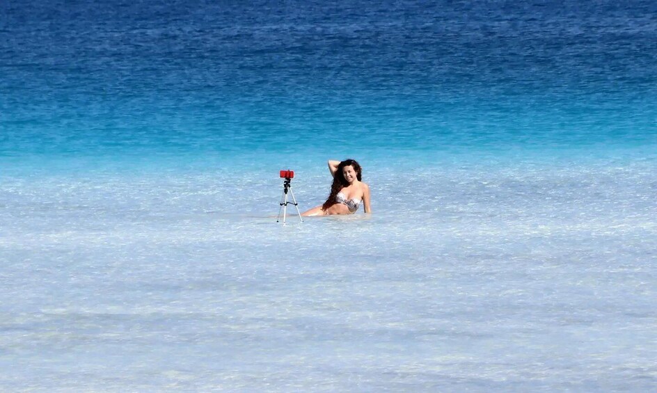 A person in a bikini in clear blue water with a tripod. 3