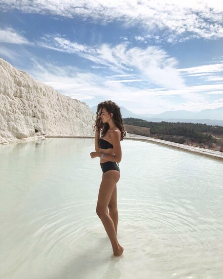 A person standing in a mineral-rich pool with white travertine formations in the background. 2