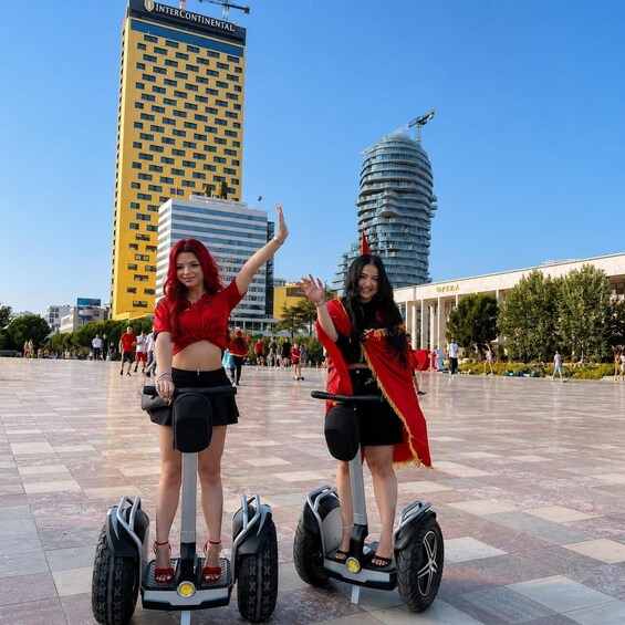 Two people on hoverboards in an urban square with modern buildings in the background. 3
