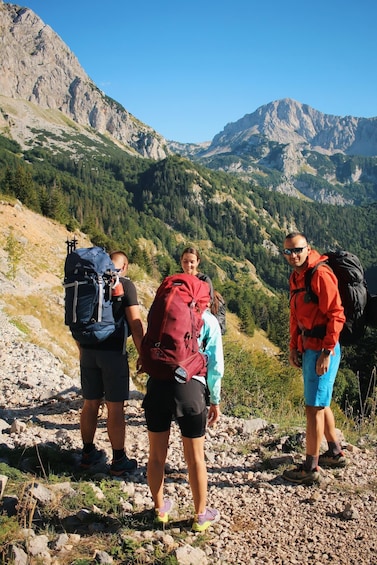 Three hikers on a rocky mountain trail with a mountainous landscape in the background. 5