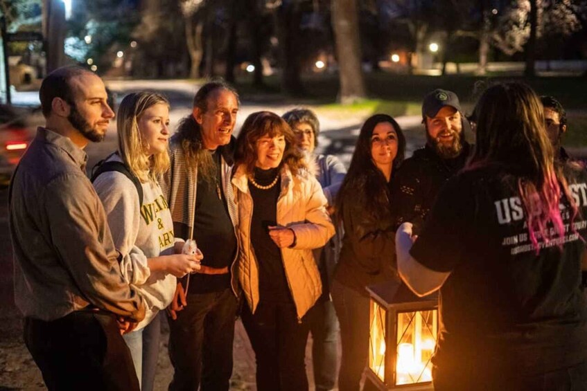 A group of people gathered around a lit lantern in a park at night. 4