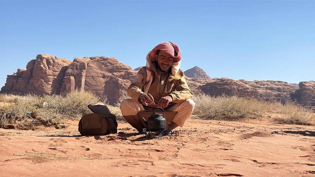 A person sitting on the ground in a desert with a kettle, a backpack, and a tent. 2