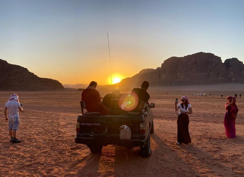 A desert landscape with a sunset, a vehicle, and people. 1