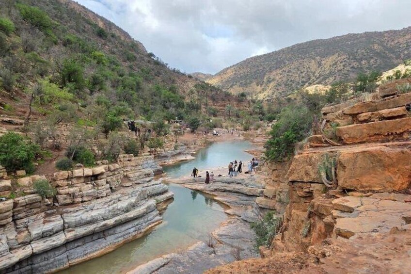 A river canyon with layered rock formations and a group of people near the water. 1