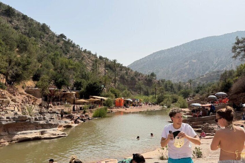 A river with people swimming and standing on the banks, surrounded by hills and sparse vegetation. 4