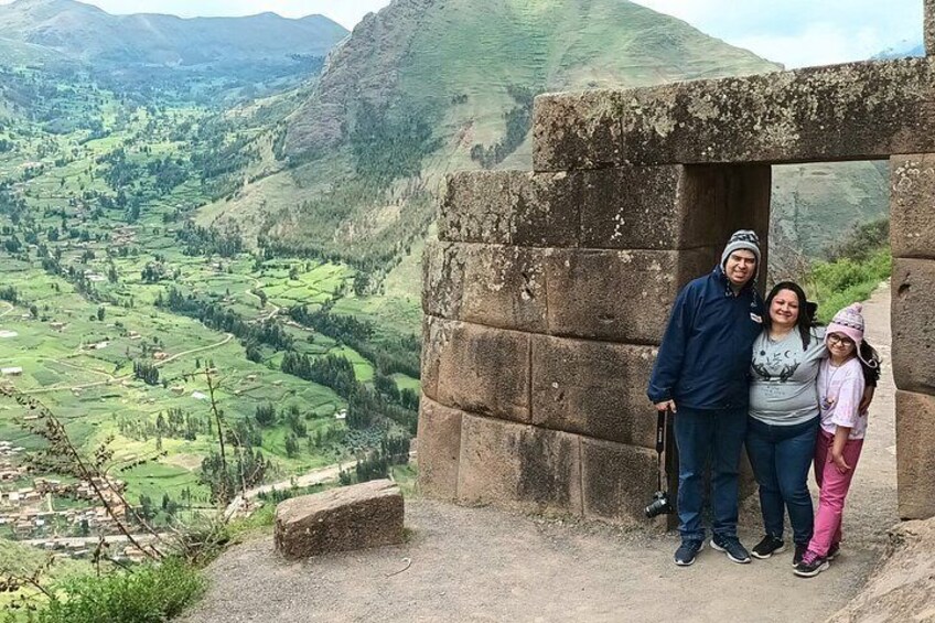 A family standing in front of a stone structure with a view of a valley and mountains in the background. 3