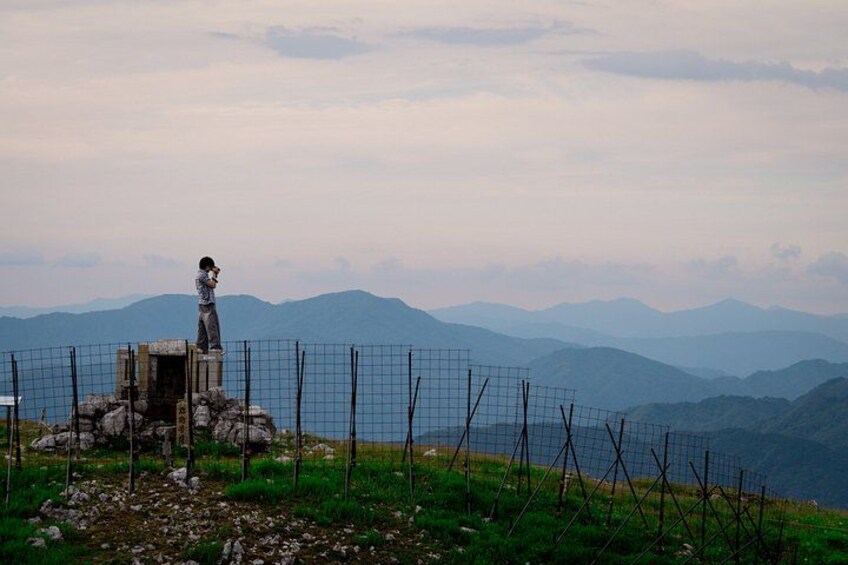 A statue on a rocky outcrop with a wire fence in the foreground and mountains in the background. 5