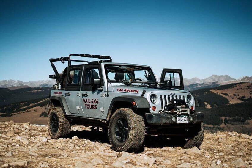 A 4x4 vehicle with 'VAIL 4X4 TOURS' written on the side, parked on rocky terrain with mountains in the background. 2