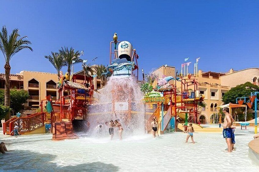 A water park with a large water fountain, palm trees, and a building with multiple levels. 4
