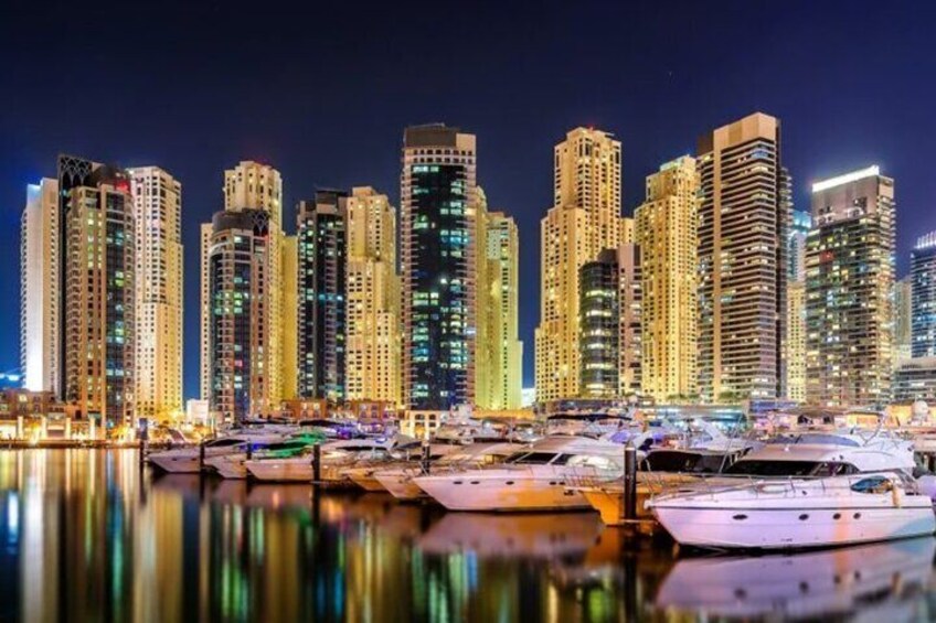 A marina with yachts docked in front of a city skyline at night. 4