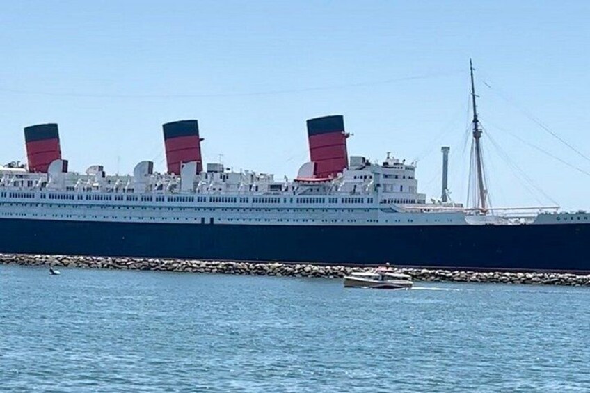 Een groot schip met drie opvallende schoorstenen, afgemeerd aan een pier met rustig water. 3