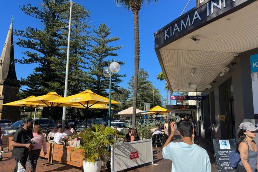 Outdoor seating with yellow umbrellas, a building with a sign reading 'KIAMA INN,' and a church spire in the background. 5