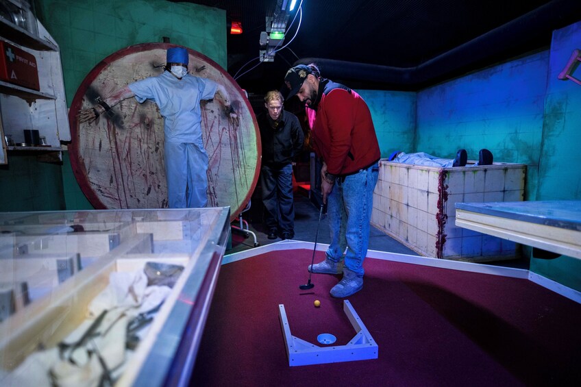 A dimly lit room with a billiards table, a large circular object resembling a target, and a display case with various items. 5