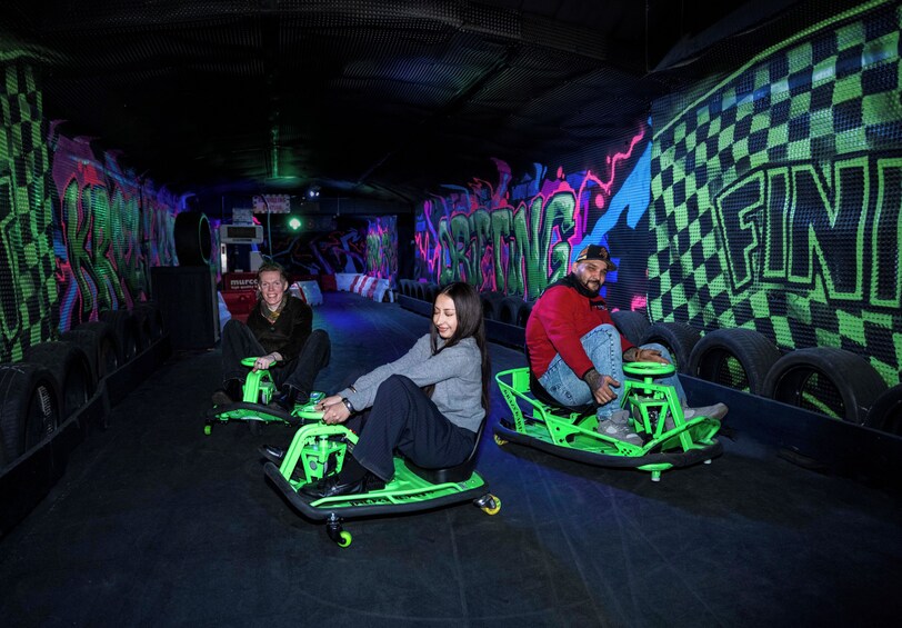 Three people on neon green go-karts in a dimly lit indoor space with graffiti walls. 4