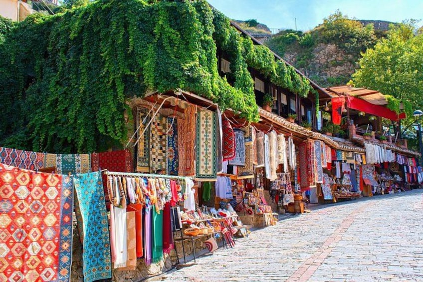 A street market with colorful textiles and rugs displayed on stalls. 2