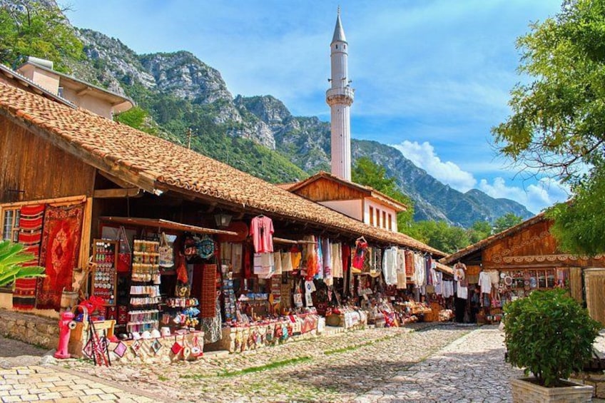A cobblestone street with shops, a mosque, and mountains in the background. 1