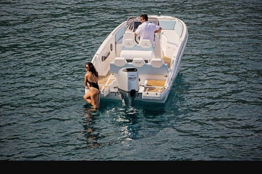 A small motorboat on calm water with a person steering and another person sitting at the back. 3