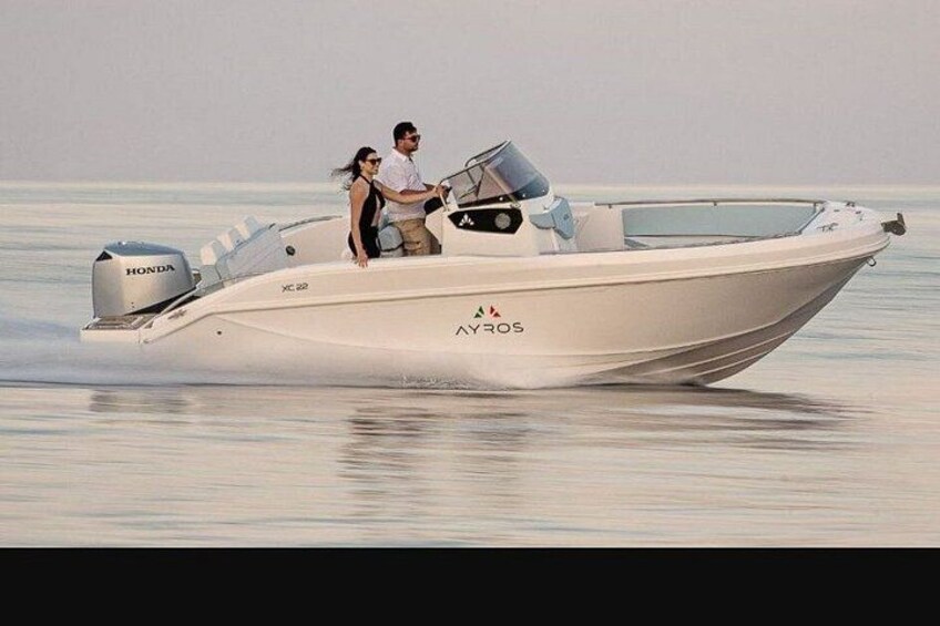A white boat with 'AYROS' branding, a man and a woman on board, and calm water. 2