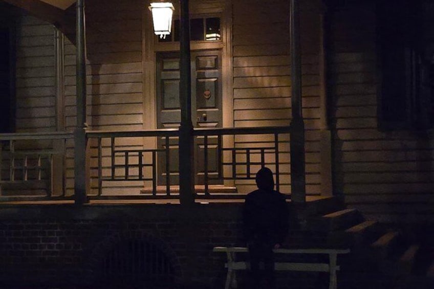 A person sitting on a bench outside a wooden building at night. 4