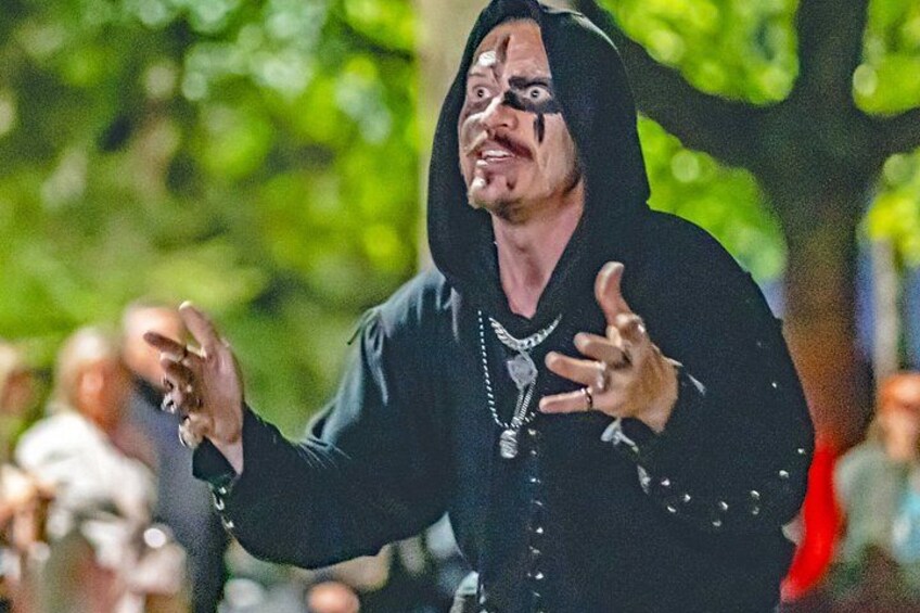 A person in black attire with a hood, gesturing with hands. 2