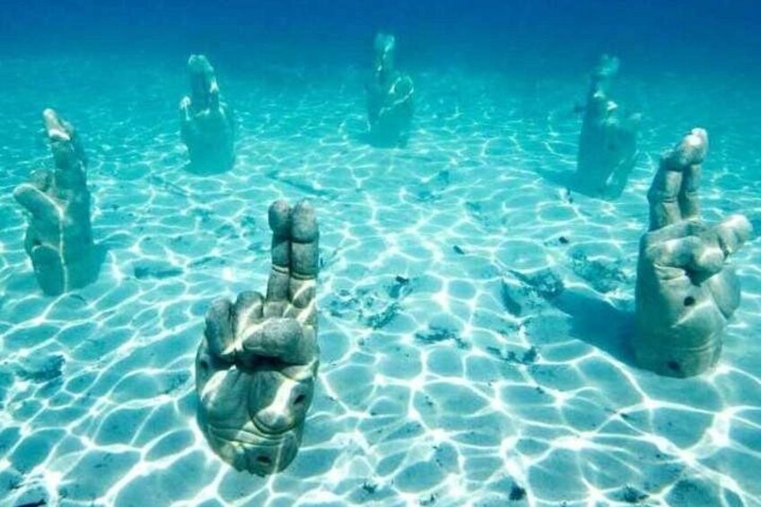 Underwater sculptures resembling hands in a clear blue sea. 3