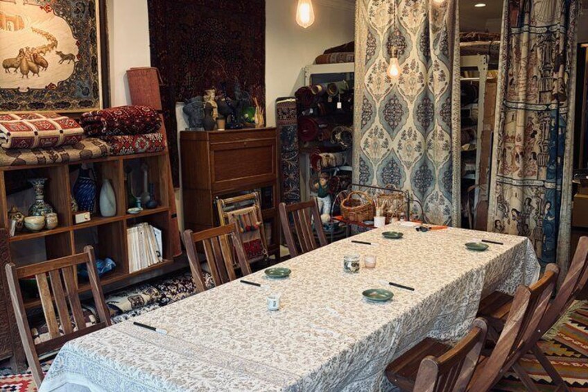 A dining table with a lace tablecloth, wooden chairs, and a patterned wall tapestry. 1