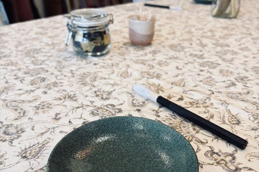 A green plate on a table with a black and white brush and a small jar in the background. 5