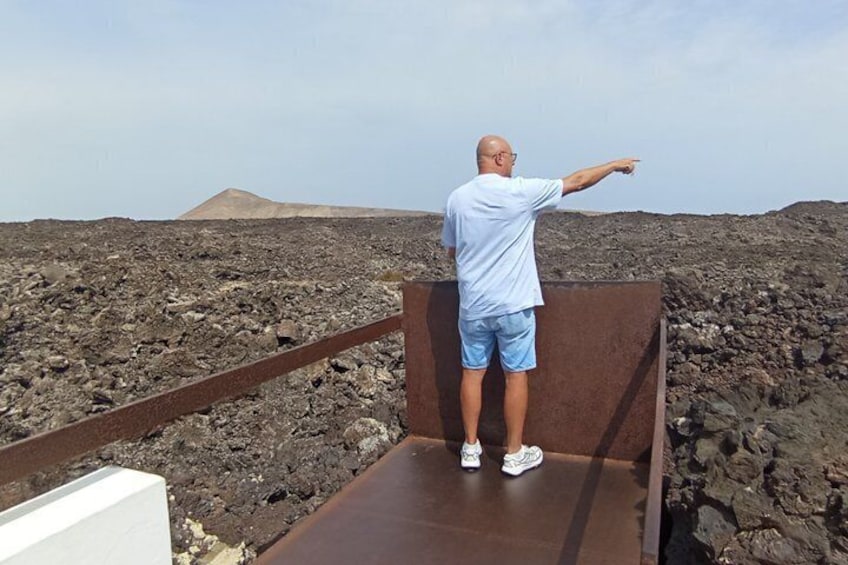 A man standing on a metal platform pointing towards a volcanic landscape. 3
