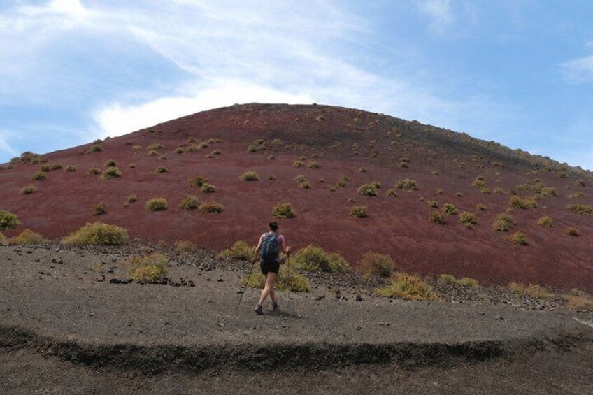 A person hiking on a red volcanic terrain with sparse vegetation. 4