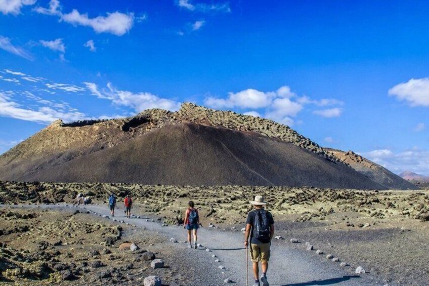 A group of hikers on a rocky trail with a large hill in the background. 1