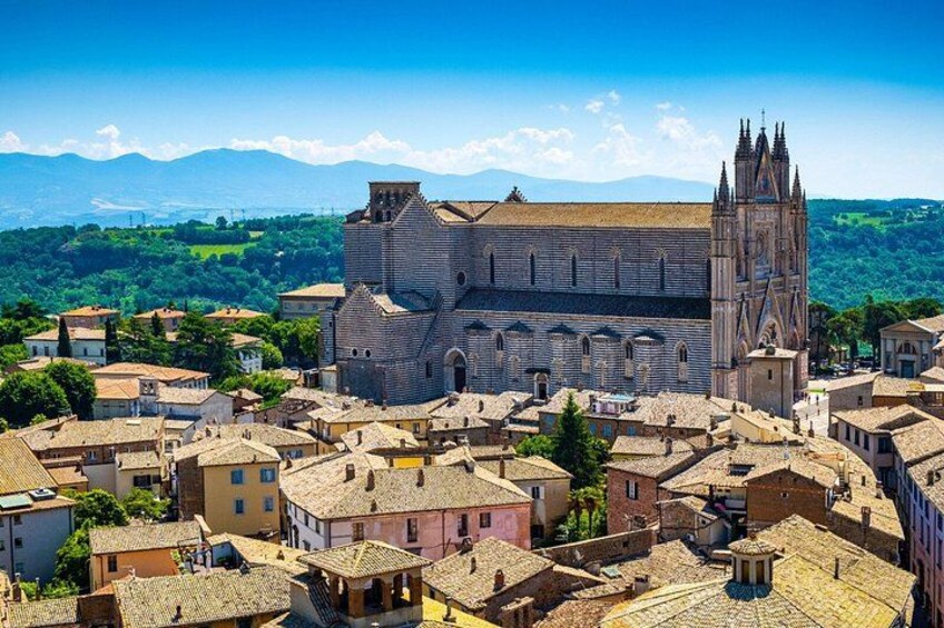A historic town with a prominent church featuring a tall bell tower, surrounded by traditional buildings and a mountainous backdrop. 1