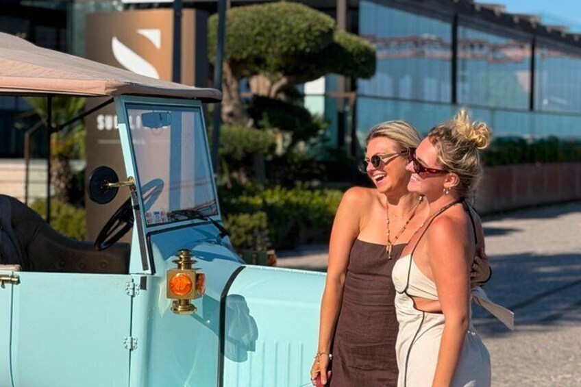 Two people standing next to a light blue vintage car with a sunroof. 1