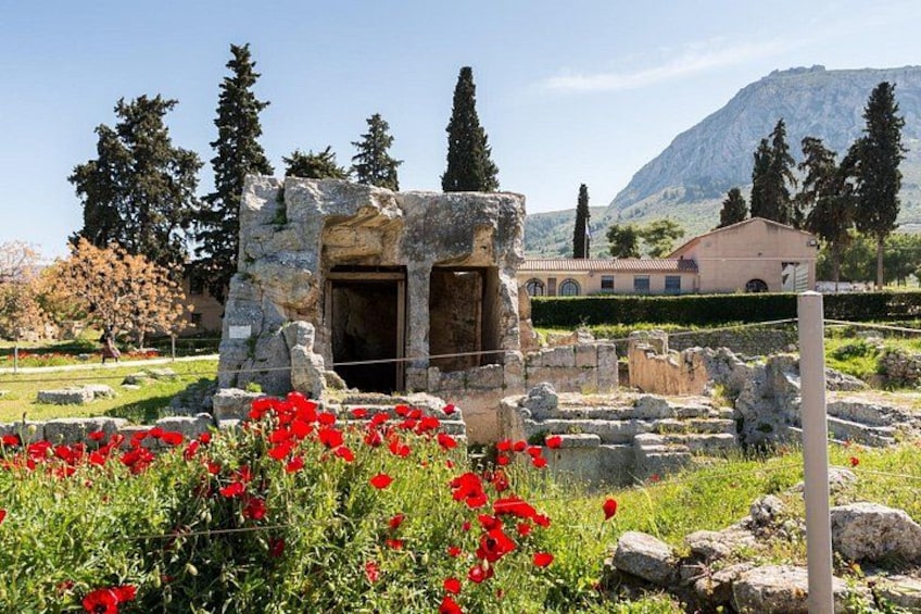 Ancient ruins with red flowers in the foreground, a building in the background, and a mountainous landscape. 5