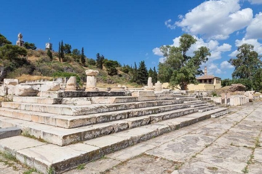 Ancient ruins with stone steps and columns, set against a backdrop of trees and a clear sky. 2